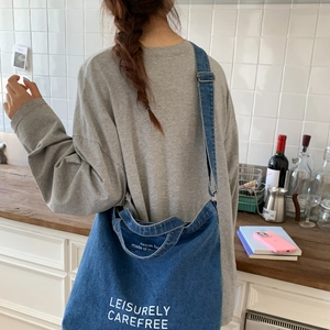 Detailed close-up of blue denim tote bag featuring white artistic lettering and texture