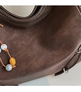 Détail d'un sac cabas en cuir marron avec surpiqûres blanches et pendentif en perles