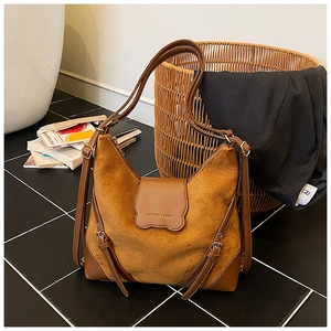 Détail du sac bandoulière en daim marron avec rabat festonné et logo de mode embossé