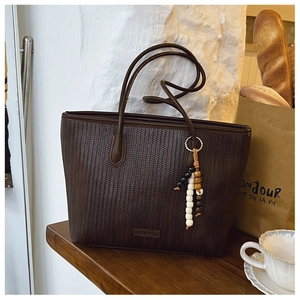 Detail of dark brown woven tote bag with bohemian bead charm on rustic wooden table