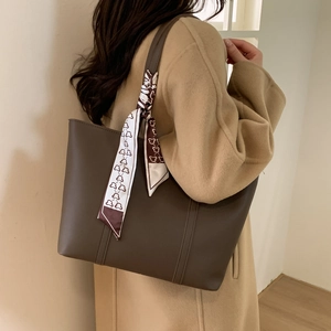 Close-up of a large brown leather tote bag with a decorative bear pattern scarf on handle