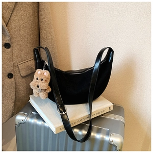 Detail of a black half-moon hobo bag with a plush dog charm on a silver suitcase