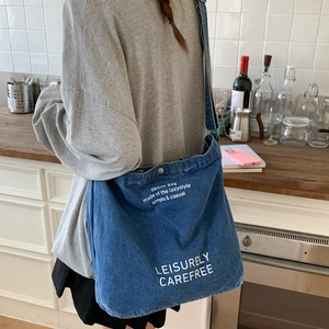 Large denim shoulder bag with white lettering shown from a side view on a model