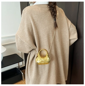 Détail du sac croissant doré avec textures géométriques sur pull en maille beige