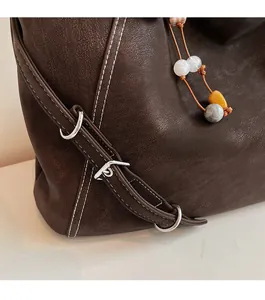 Détail du sac cabas en cuir marron foncé avec coutures blanches et boucles métalliques