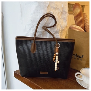 Detail of woven tote bag with dark brown leather handles and wooden beaded ornament