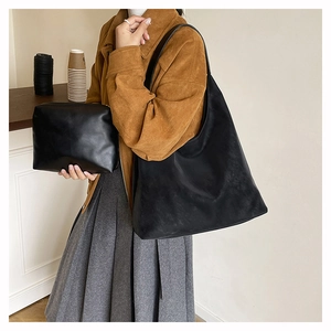 Classic black hobo tote bag and matching pouch set worn by a model in a warm setting