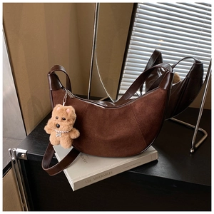 Detail of suede crescent bag with smooth leather trim and cute puppy charm on a book