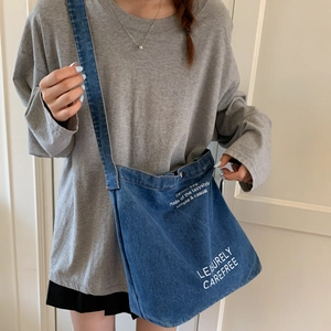 Detail of blue denim bucket bag featuring white typography print and a wide shoulder strap