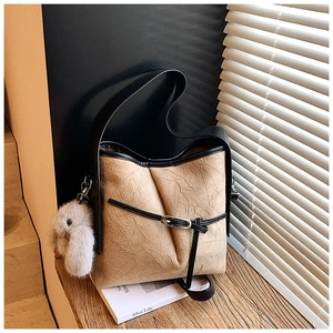 Detail of khaki bucket bag with pleated texture, black straps and white fluffy charm
