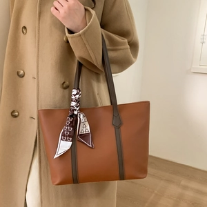 Close-up of brown leather tote bag featuring a decorative printed silk scarf on handle