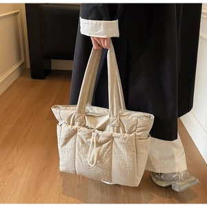 Detail of beige quilted tote bag showing side drawstring pockets and nylon texture