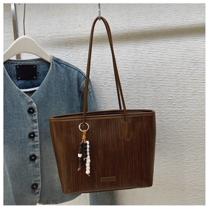 Detail of coffee brown tote bag with textured finish and wooden bead charm accessory