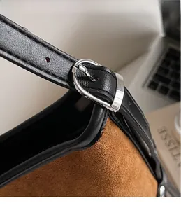 Macro view of adjustable leather strap with silver buckle on brown suede tote bag
