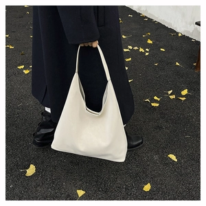 Close-up of a cream white leather hobo bag worn with a dark coat on a street