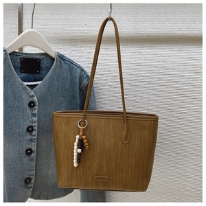 Close-up of brown woven tote bag with wooden bead charm and silver brand logo plate