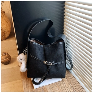 Detail of black pleated texture shoulder bag with golden buckle and plush rabbit charm