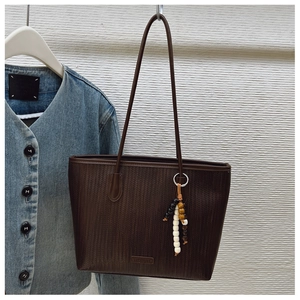 Detail of dark brown woven tote bag featuring a brand plate and wooden beaded charm