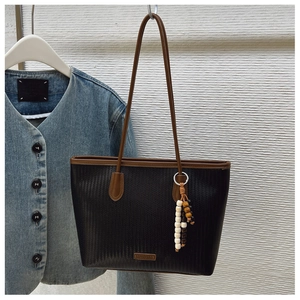 Black woven tote bag with brown leather straps and colorful bead pendant detail