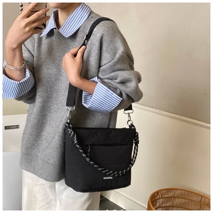 Detail of black quilted crossbody bag with rope handle and adjustable strap worn by model