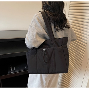 Detail of black puffer tote bag with multi-pocket design and drawstring metal buckle