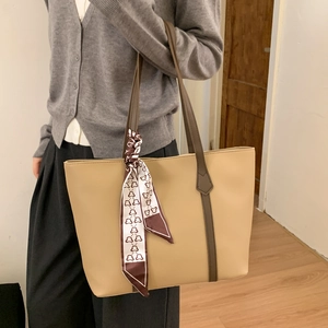 Detailed close-up of a large khaki tote bag with dark brown handles and silk scarf detail
