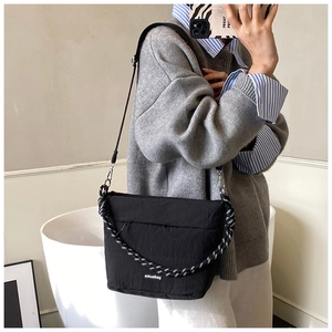 Detail of black quilted puffy crossbody bag featuring braided rope handle and woven logo