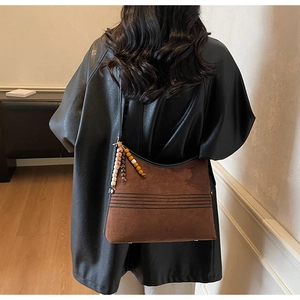 Detailed shot of brown suede tote bag featuring ethnic bead charm and stitching accents