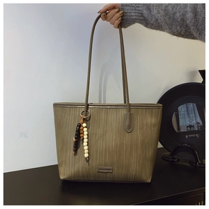 Detail of woven texture khaki tote bag with beaded tassel and brand logo plate