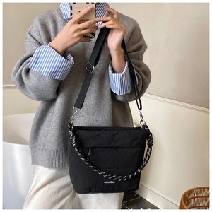 Quilted black crossbody bag featuring a woven handle and adjustable nylon shoulder strap