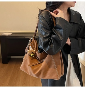 Detailed close-up of brown suede hobo tote bag with white stitching and bear charm