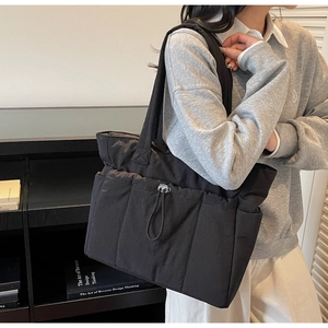 Detail of black quilted tote bag with drawstring feature and waterproof nylon texture