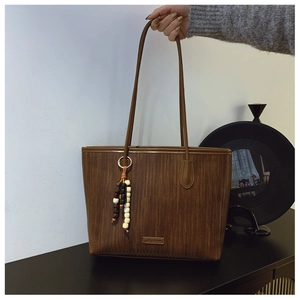 Detailed view of brown woven tote bag with beaded tassel and brand logo plate