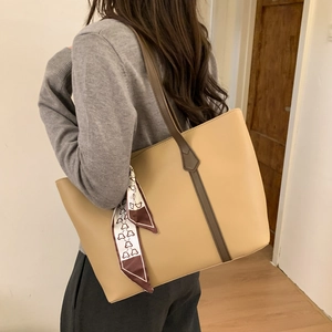 Detail of minimalist tote bag in beige leather with silk scarf and bear print accent