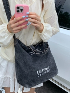 Large black washed denim tote bag with leisure lettering shown on model in daylight