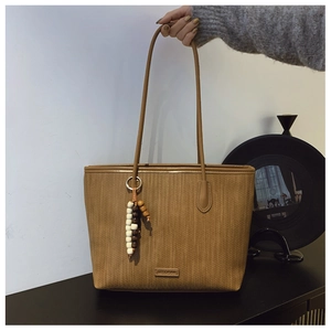 Detailed shot of brown woven tote bag featuring a wooden bead tassel and metal logo