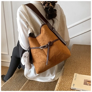 Detail of caramel bucket bag with wrinkled texture and a white plush rabbit charm