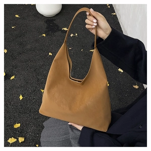 Detailed close-up of a minimalist brown leather hobo bag held in a street setting