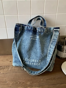 Blue denim tote bag with leisure text and adjustable strap on a wooden table
