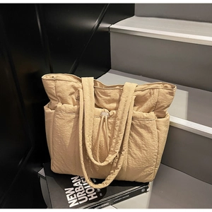 Detail of quilted beige nylon tote bag showing drawstring texture and side pocket design