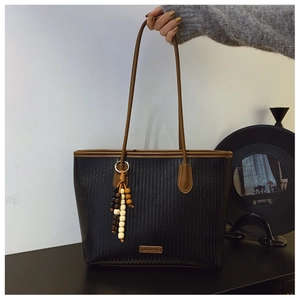 Close-up of black woven tote bag with brown leather straps and colorful beaded tassel