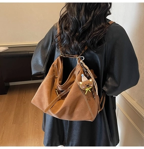 Rear view of brown suede shoulder bag with contrast stitching and a plush bear charm