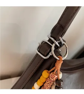Detail view of brown faux leather shoulder bag with adjustable strap and colorful wood bead tassel