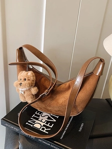 Brown leather hobo shoulder bag with cute teddy bear charm on minimalist background