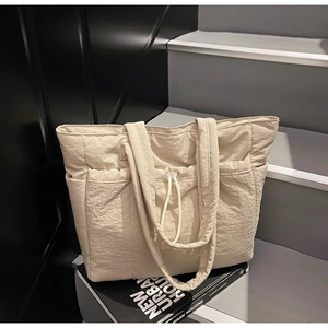 Detail of off-white padded tote bag featuring quilted texture and side drawstring pockets