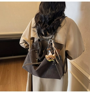 Detail view of brown suede tote bag with white contrast stitching and a small bear charm