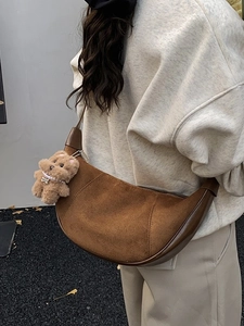 Brown suede hobo bag with teddy bear charm shown from a side view in an outdoor setting