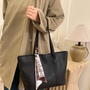 Detail of a black leather tote bag with a patterned silk scarf on a trench coat model