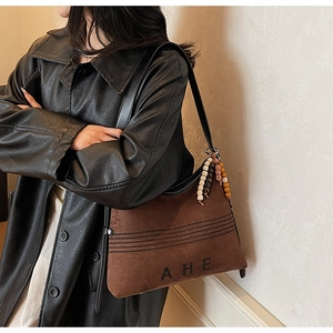 Detail of a brown suede tote bag featuring black AHE lettering and colorful beaded charm