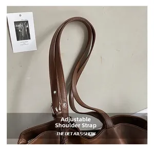 Detail of adjustable shoulder strap on brown suede tote bag with metal buckle and eyelets